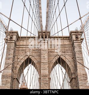Details der Rooklyn Bridge bei Sonnenuntergang und Abenddämmerung aus nächster Nähe von Kabeln und Steinbögen in Lower Manhattan New York City Stockfoto