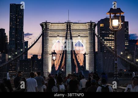 Brooklyn Bridge Fußgänger, die bei Sonnenuntergang am Abend und in der Nacht spazieren gehen, sehen Sie die Kabel und Steinbögen in Lower Manhattan, New York City Stockfoto
