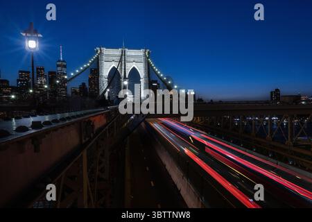 Brooklyn Bridge Traffic - Autos bei Sonnenuntergang Abend und Einbruch der Dunkelheit - Zeitverzögerungsbewegung verschwimmen Steinbögen in Lower Manhattan New York City mit Skyline Stockfoto