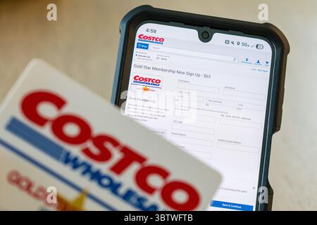 Salt Lake City, Utah, 15. Juli 2025 – Costco Gold Star-Mitgliedskarte wird vor dem Telefonbildschirm gehalten und die Anmeldeseite für Costco.com ist geöffnet. Stockfoto