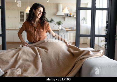 Gemütliches Wohndekor, Herbst- oder Winterleben. Positive Millennial Frau, die zu Hause warmes Karli auf die bequeme Couch legt Stockfoto