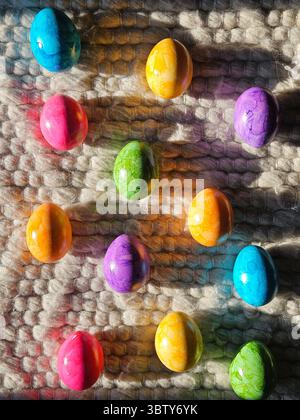 Bunte Ostereier auf strukturiertem Wollteppich im Sonnenlicht. Lebhafte Frühlingsferien im Hintergrund. Hochwertige Fotos Stockfoto