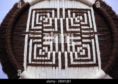 Geometrische Wandkunst in Braun und weiß aus Makramee Eine handgefertigte Makramee-Wand mit geometrischem braunem und weißem Muster, die präzise gewebt wurde. Stockfoto