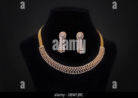 Elegante Gold- und Rautenkette mit passenden Ohrringen auf schwarzem Samtdisplay Stockfoto