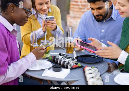 Freunde, die Sushi und Telefone teilen Stockfoto