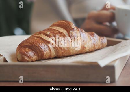 Frisch gebackenes Croissant auf Holztablett im Café-Ambiente Stockfoto