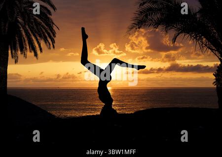 Friedliche Silhouette einer Frau, die Yoga am Rande einer ruhigen Küste während eines lebendigen Sonnenuntergangs praktiziert. Dieses beruhigende Bild symbolisiert Achtsamkeit, inneres Gleichgewicht, spirituelles Wachstum und Verbindung mit der Natur. Ideal für Wellness-Branding, Meditationsinhalte, Yoga-Retreats und inspirierende Lifestyle-Visuals. Stockfoto