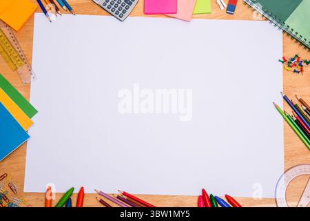 Leeres Blatt Papier liegt flach auf einem Holzschreibtisch in flachem Design, mit farbenfrohen Schreibwaren Stockfoto