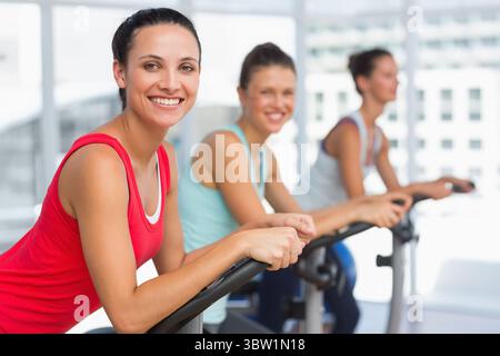 Drei Frauen radeln in einem flachen Fitness-Studio mit Stadtfenstern und Heimtrainer Stockfoto