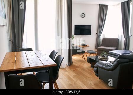 Ein moderner Wohnbereich mit Ledersofa, fernseher, Holzmöbeln und Vorhängen, wunderschön beleuchtet durch natürliches Licht, schafft eine gemütliche und gemütliche Atmosphäre Stockfoto