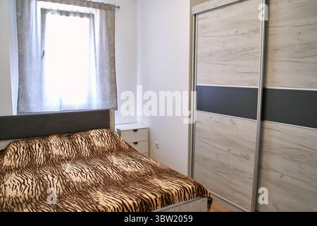 Ein gemütliches Schlafzimmer mit Tiermotiv und einem modernen Holzschrank. Der Raum verfügt über Tageslicht, eine minimalistische Einrichtung und eine ruhige Atmosphäre Stockfoto