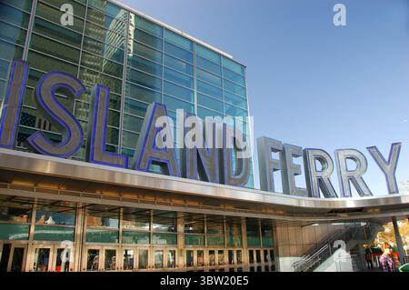 Moderner Staten Island Fährhafen in New York City an einem sonnigen Tag, bei dem Menschen spazieren gehen und die Glasfassade reflektiert wird Stockfoto