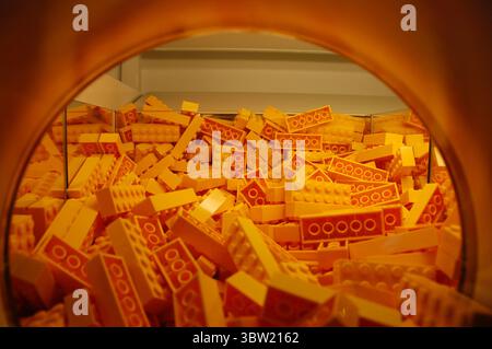 Nahaufnahme eines gelben LEGO-Backsteinbehälters an der Pick-a-Brick-Wand eines LEGO Stores mit leuchtenden Kunststoffbausteinen in einem orangefarbenen Display Stockfoto