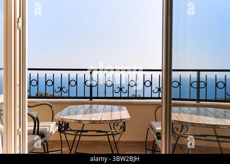 Das Bild zeigt einen ruhigen Balkon mit kunstvoll verzierten Geländern und bietet einen ruhigen Blick auf das Meer. Gemütliche Sitzgelegenheiten laden zum Entspannen ein, unter klarem Himmel, perfekt für einen Stockfoto