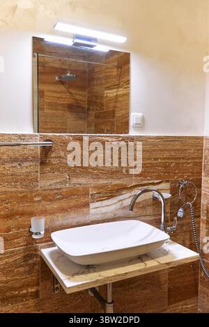 Dieses moderne Badezimmer verfügt über luxuriöse Marmorfliesen, ein elegantes weißes Waschbecken, moderne Armaturen und eine elegante Beleuchtung für einen minimalistischen, stilvollen Stil Stockfoto