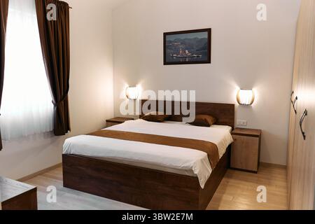 Ein gemütliches, minimalistisches Schlafzimmer mit Holzrahmen, warmer Beleuchtung und heiterer Wandmalerei schafft eine ruhige und einladende Atmosphäre für erholsame Erholung Stockfoto