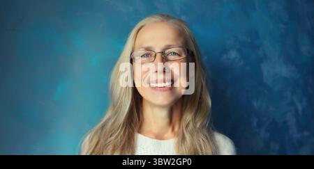 Porträt einer glücklichen, lächelnden, selbstbewussten, Reifen Frau mit Brille, die in die Kamera schaut. Grauhaarige Frau in Casual auf blauem Hintergrund Stockfoto