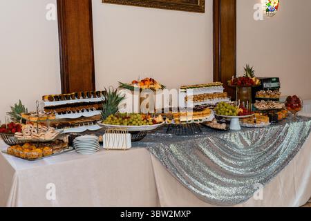 Luxuriöses Dessertbuffet mit einer großen Auswahl an Gebäck, frischem Obst und silberner Paillettentischdecke in einer Veranstaltungsumgebung, ideal für Hochzeitsfeiern Stockfoto