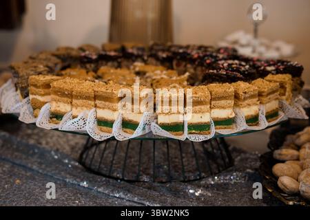 Eine wunderschöne Präsentation von verschiedenen quadratischen Kuchen auf einem dekorativen silbernen Ständer mit weißen Papierdeckchen, die eine luxuriöse Essenspräsentation einfangen Stockfoto