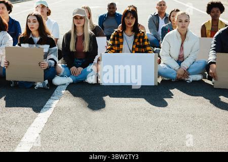 Eine sitzende Gruppe verschiedener junger Erwachsener mit leeren Schildern, die an einer friedlichen Demonstration teilnehmen und ihre Solidarität und ihren Aktivismus symbolisieren, um Werbung zu machen Stockfoto