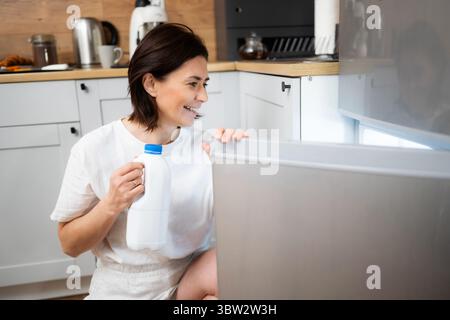 Fröhliche Frau in der Küche, die Eine Milchflasche aus dem Kühlschrank holt Stockfoto