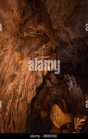 Besucher bestaunen die komplizierten Höhlenformationen, die von sanfter Beleuchtung beleuchtet werden. Die felsigen Texturen und Schatten schaffen eine faszinierende Atmosphäre tief Stockfoto