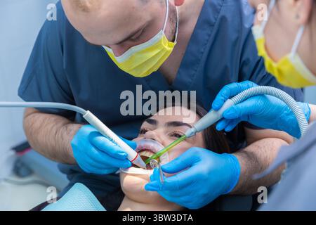 Zahnarztpraxis mit modernen Techniken: Zwei Zahnärzte führen in der Zahnarztpraxis mit fortschrittlichen Geräten und Schutzmitteln die Behandlung des Patienten durch Stockfoto