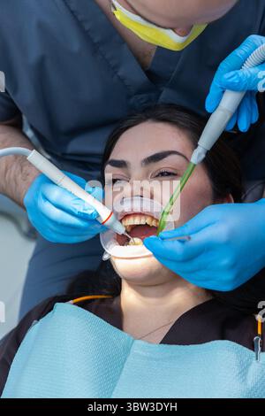 Zahnärztlicher Eingriff im Gange: Nahaufnahme eines Patienten, der eine zahnärztliche Behandlung mit Werkzeugen und Händen eines Zahnarztes mit Schutzausrüstung erhält Stockfoto