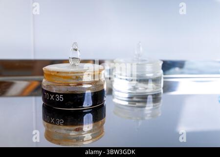 Zwei Laborbehälter mit unterschiedlichen Flüssigkeiten, die auf einer Metalloberfläche reflektiert werden und Farbvariationen und wissenschaftlichen Kontext in einem kontrollierten Bereich darstellen Stockfoto