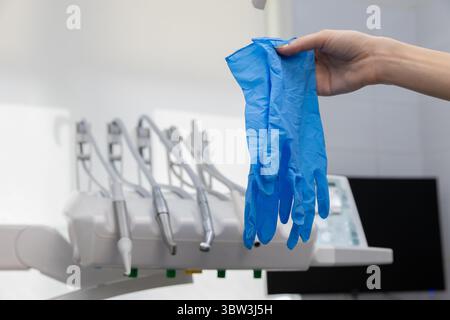 Eine Nahaufnahme einer Hand, die blaue Chirurgenhandschuhe in einer Zahnklinik hält, mit Dentalwerkzeugen im Hintergrund Stockfoto