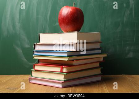 Verschiedene Bücher und roter Apfel auf Holztisch in der Nähe der Tafel Stockfoto