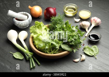 Verschiedene aromatische Kräuter in Schüssel, Saucen und Gewürze auf dunkel strukturiertem Tisch, Nahaufnahme Stockfoto