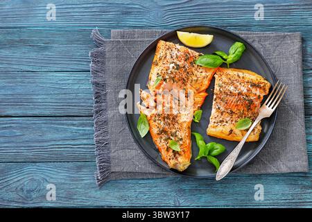 Gegrillte ganze Lachsfilets mit Haut auf einem Teller mit frischem Basilikum, Zitronenscheiben, Gabel auf Holztisch, Draufsicht, freier Platz, flach liegend, Nahaufnahme, nicht Stockfoto