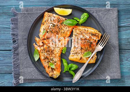 Gegrillte ganze Lachsfilets mit Haut auf einem Teller mit frischem Basilikum, Zitronenscheiben, Gabel auf Holztisch, Draufsicht, flach liegend, Nahaufnahme, nicht KI generieren Stockfoto