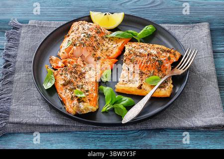 Gegrillte ganze Lachsfilets mit Haut auf einem Teller mit frischem Basilikum, Zitronenscheiben, Gabel auf Holztisch, horizontal von oben, Nahaufnahme, nicht AI Gener Stockfoto