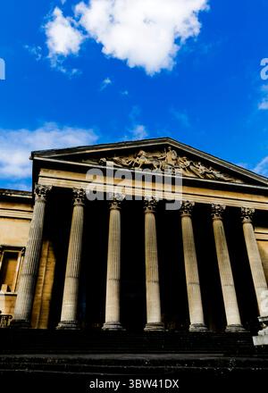 Eine Niedrigwinkelaufnahme eines Gebäudes mit großen Säulen und einem detaillierten Fries unter einem blauen Himmel mit Wolken. Stockfoto