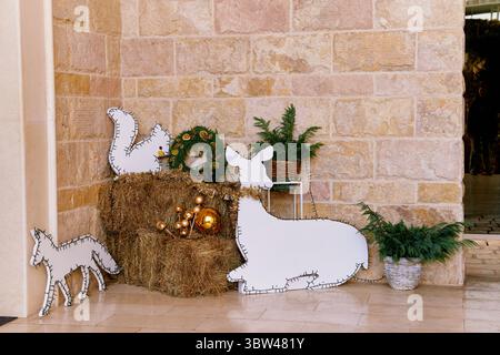 Ein gemütliches rustikales Urlaubsangebot mit Heu, Kranz, Kiefer und Tierausschnitten, die ein charmantes Bauernhaus-Ambiente vor einer strukturierten Steinmauer schaffen. Stockfoto