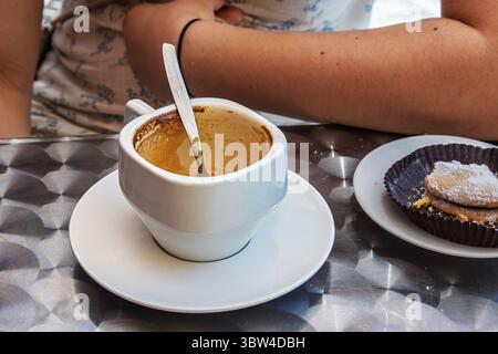 Fertige Espresso-Tasse, Löffel und italienisches Pudergebäck auf Metall-Kaffeetisch. Junge Frau Arm im Hintergrund. Selektiver Fokus Stockfoto