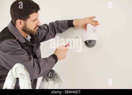 Techniker auf der Leiter, der die Dome-Sicherheitskamera mit einem Schraubendreher für die Montage der Befestigungsteile installiert. Stockfoto