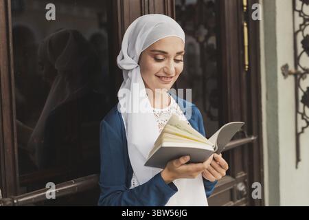 Porträt einer jungen muslimischen Frau, die im Freien ein Hijab-Lesebuch trägt Stockfoto