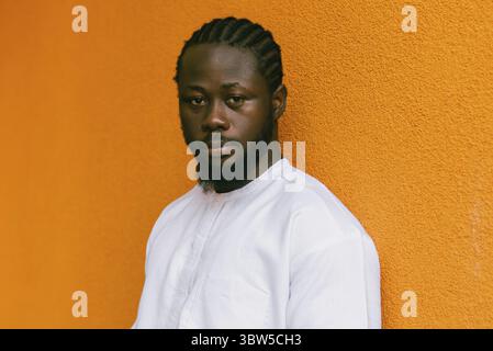 Nahaufnahme Porträt eines afroamerikanischen Mannes, der draußen in ethnischer Dashiki-Kleidung lächelt, in der orangefarbenen Wand der Sommerstraße. Millennial Generation Student Stockfoto