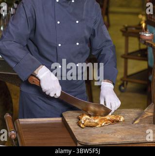 Koch schneidet ein Hühnerfleisch mit einem Spaltmesser auf dem Holzplatte Stockfoto
