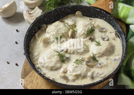 Hausgemachte Fleischbällchen in Sauerrahmsauce mit Pilzen in einer Pfanne auf Stein- oder Schiefertisch Stockfoto