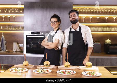 Glücklicher Koch und sein Kollege stehen in der Küche und schauen in die Kamera - Essen und Restaurantkonzept Stockfoto