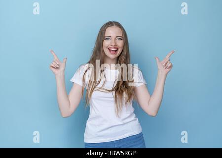 Hey, sieh mal. Ein lächelndes, schönes weibliches Model, das mit den Fingern in einen leeren Raum zeigt Stockfoto
