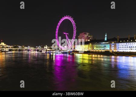 Ein atemberaubender Blick auf das London Eye, das nachts in leuchtenden Farben leuchtet, ergänzt durch ruhige Reflexionen der Themse Stockfoto