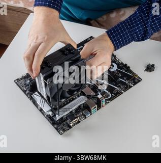 Die Hände eines Mannes, der einen Lüfter am CPU-Kühlturm auf der Hauptplatine installiert Stockfoto