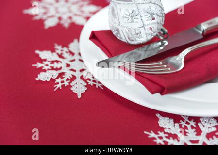 Weihnachtstisch: Silbernes Messer und Gabel, rote Leinenserviette und schöne Weihnachtskugel befinden sich auf dem weißen Porzellanteller, der sich auf einem Tisch befindet Stockfoto