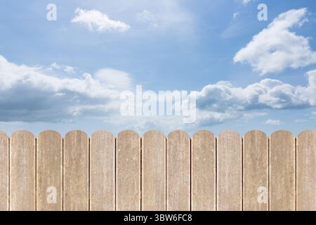 Der vertikale Holzdielen-Zaun mit flachem Design erstreckt sich unter dem hellblauen Himmel mit Wolken Stockfoto