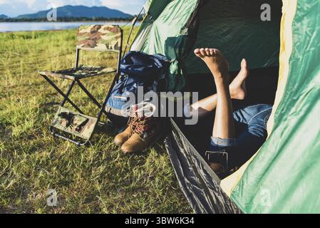 Nahaufnahme von Frau Beine entspannen in camping Zelt mit Bergsee und Wiese und Wiese Hintergrund. Lebensstile und Personen Konzept. Camping und p Stockfoto